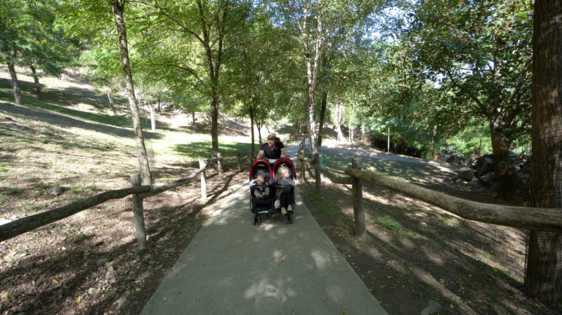 Man in a hat pushing a stroller up a steep inclined paved walking path