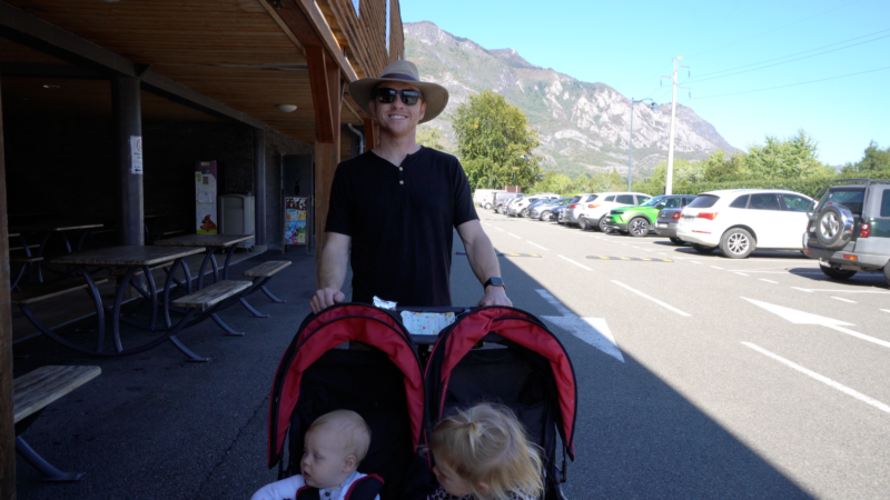 Man standing with a stroller in front of zoo entrance with a mountain in the background